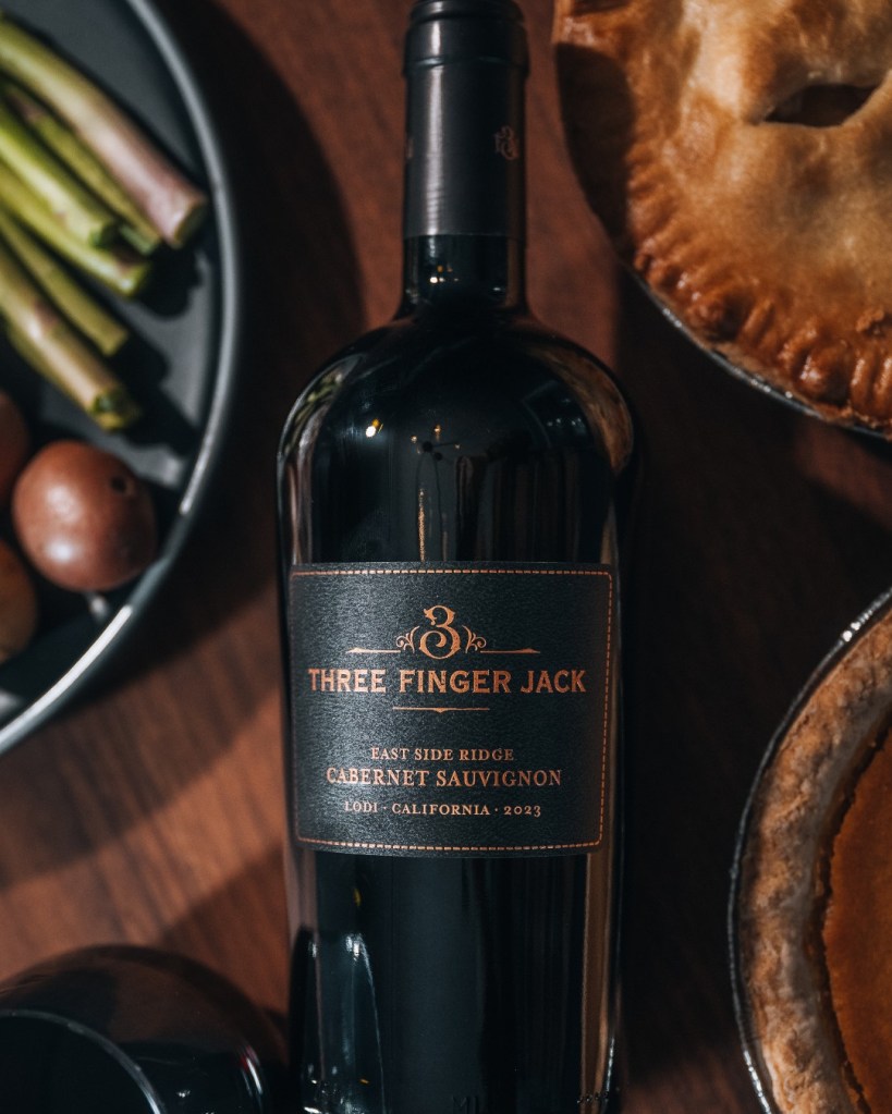 A bottle of Three Finger Jack Cabernet Sauvignon on a table with spices and pies