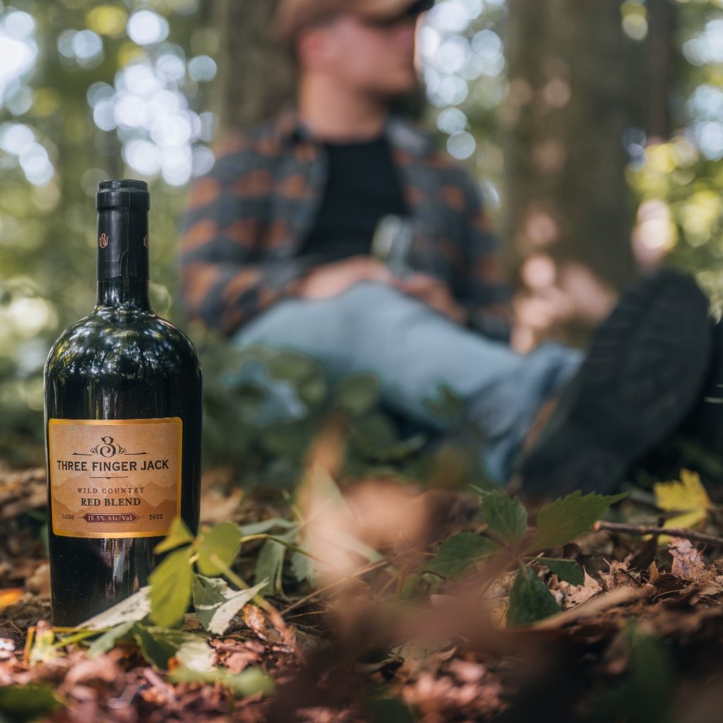 A bottle of Three Finger Jack Wild Country Red Blend in the fall leaves out in the woods